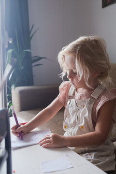  little girl drawing with felt-tip pen on paper at table near window