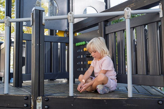  little girl sitting on wooden floor playing alone at outdoor playground