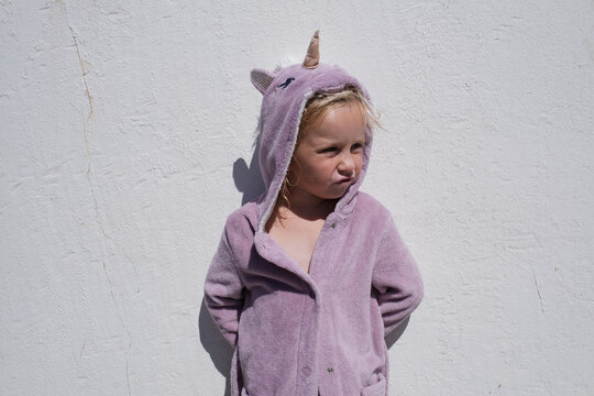 little girl in funny unicorn hooded bathrobe standing against white wall
