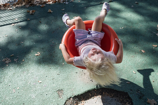little girl spinning upside down in bowl roundabout seat at outdoor playground