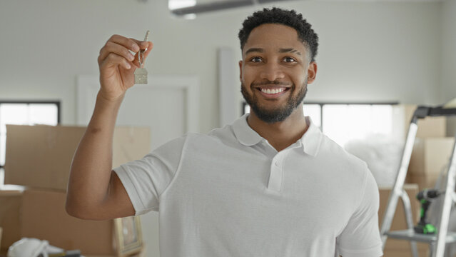 Man holds key in raised hand and points finger to key inside a building with packed moving boxes, ladder and hardhat; moving day joy.