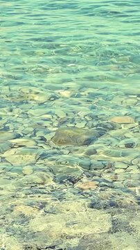 Turquoise water flows softly around a smooth stone, highlighting the peaceful interaction between land and sea in a coastal environment