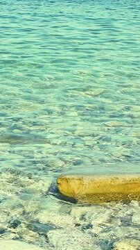 Turquoise water flows softly around a smooth stone, highlighting the peaceful interaction between land and sea in a coastal environment