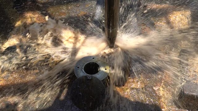Close up of long metal bailer pipe extracting crude oil with splash at Wonocolo traditional oil well, Bojonegoro, East Java, Indonesia. Traditional petroleum extraction and heritage mining process.