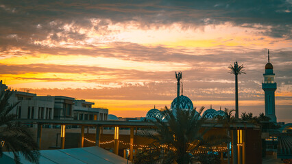 Mosque domes and minaret silhouetted against vibrant sunset sky over cityscape © Wayne