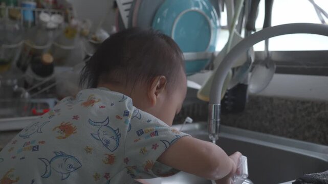 A young child enjoys playing with water at a kitchen sink, showcasing curiosity and joy. The scene captures the innocence and wonder of childhood as they explore their environment.