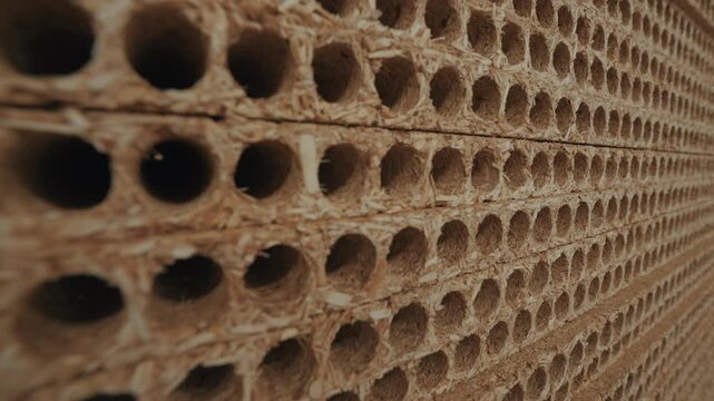 Extreme close up tracking shot along edge of stacked tubular hollow core wood chipboard particle board panels, cinematic texture