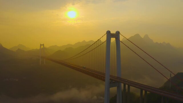 Aerial view of a suspension bridge over misty mountains at golden sunset