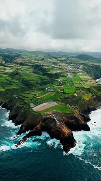 Volcanic coastline with ocean waves, rocky shore, coastal lighthouse and agricultural fields on Azores