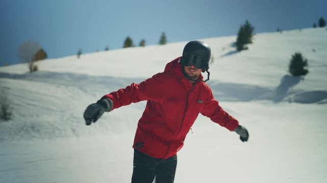 A man in a red jacket is snowboarding down a snowy mountain slope. He enjoys the winter time on the sunny hill.