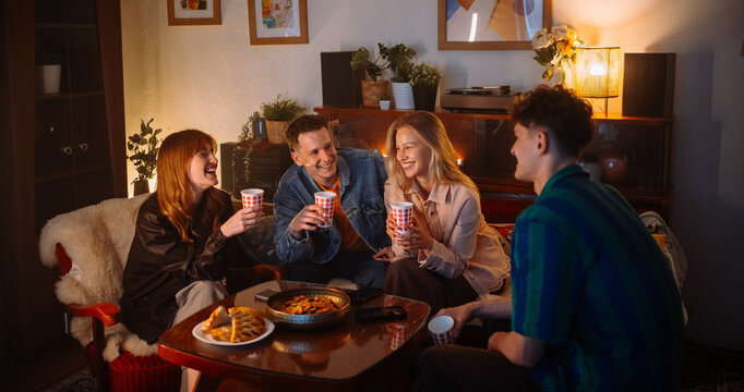 Friends Enjoying a Cozy Evening Gathering with Snacks and Drinks in Warm Ambiance