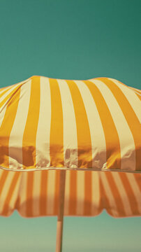 yellow and white striped beach umbrella against turquoise background, minimalist summer vacation photography with copy space for travel advertising, poster or seasonal design