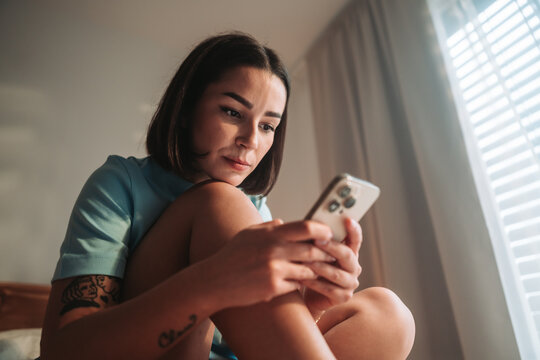 Focused Woman Absorbing Message Content, Woman With Inked Arm Studying Phone Carefully In Sunlight