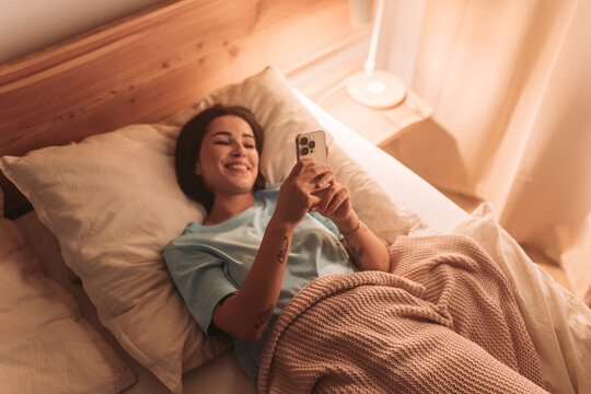 happy young lady reads cheerful text in evening, female enjoying sweet moment with phone and warm light