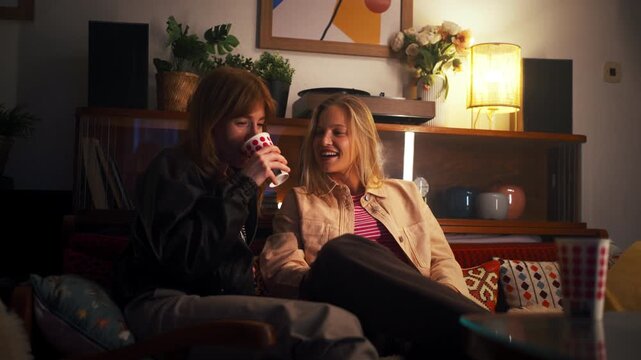 Two female friends drinking wine and talking together at home at night