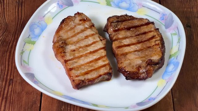 Serving of grilled pork steaks on plate on rustic table