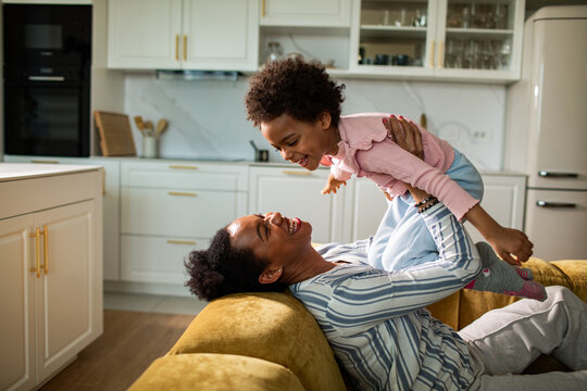 Mother lifting child on sofa in modern kitchen
