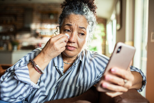 Mature woman wiping tears while looking at a phone at home