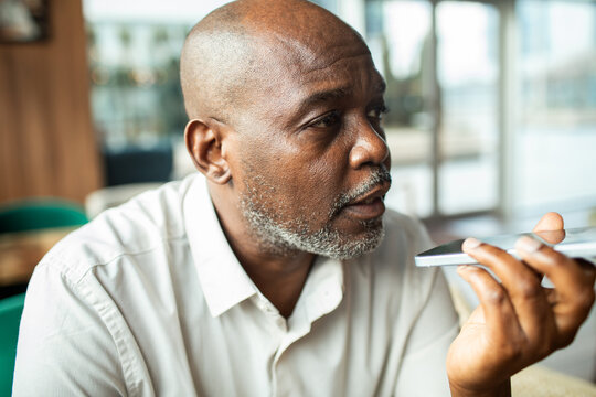 Mature man using smartphone voice command at modern cafe