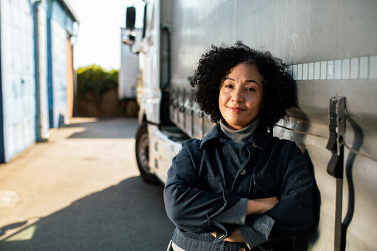 Confident female truck driver leaning on semi at distribution yard