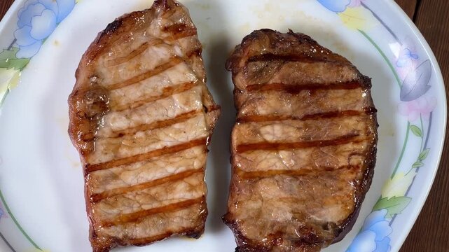 Serving of grilled pork steaks on plate on rustic table