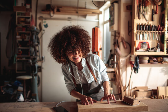 Smiling female woodworker sanding wooden board in workshop