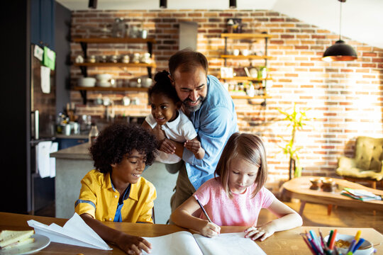 Father helping children with homework at home kitchen table
