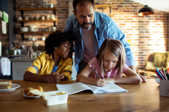 Father helping kids with homework at kitchen table