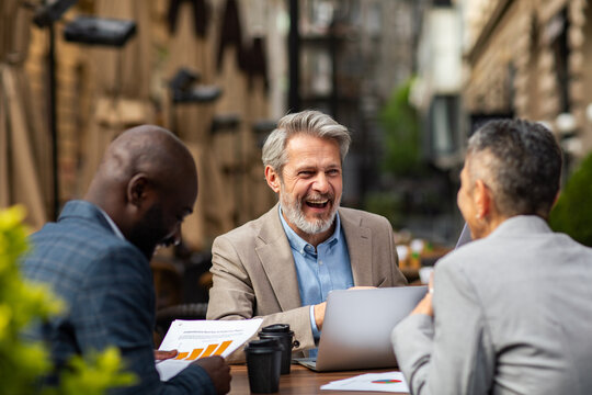 Smiling senior businessman meeting colleagues at outdoor city cafe