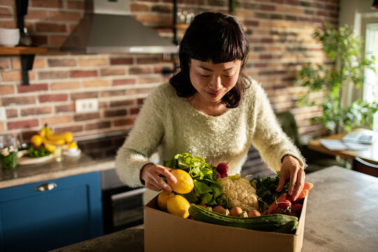 Woman unpacking fresh produce delivery in home kitchen