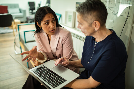 Two businesswomen discussing data on laptop in modern office