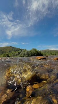 Clear River Water Flowing Over Sunlit Rocks Beneath Blue Sky