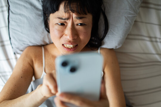 Frustrated woman looking at smartphone in bed at home