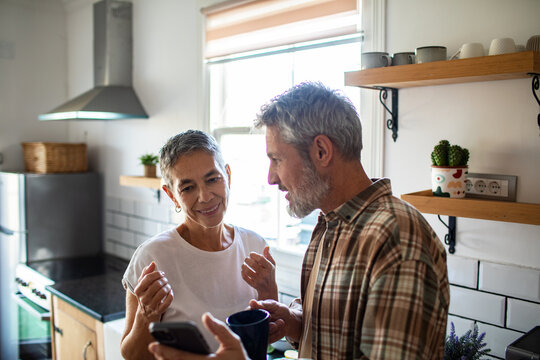 Senior couple using smartphone over morning coffee in home kitchen