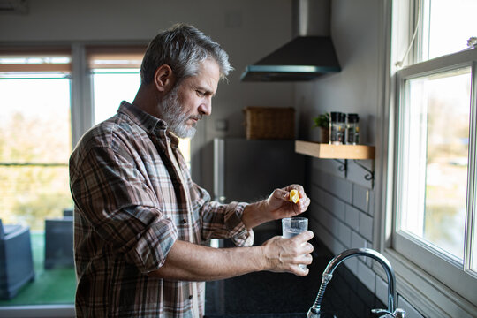 Middle-aged man squeezing lemon into water in home kitchen