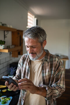 Smiling middle-aged man using smartphone in home kitchen