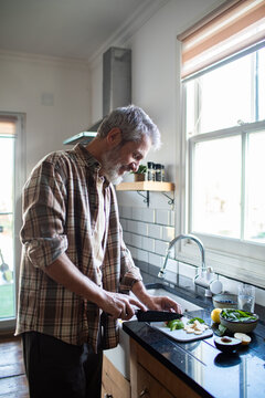 Mature man chopping fresh vegetables in home kitchen