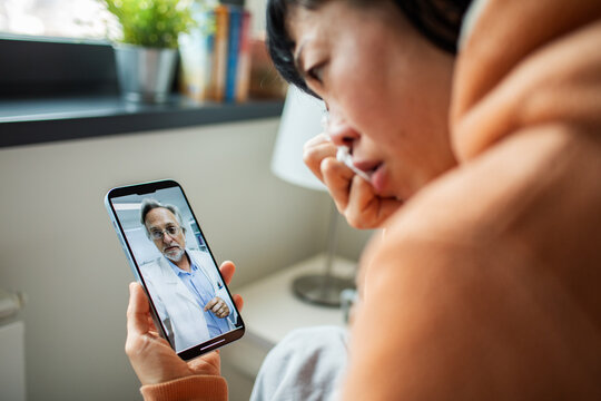Sick woman consulting doctor via smartphone at home