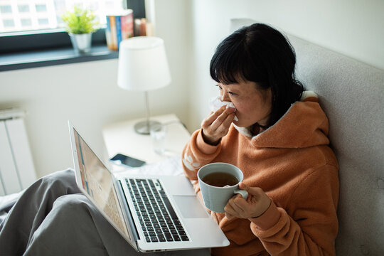 Sick woman working from bed at home with laptop and tea
