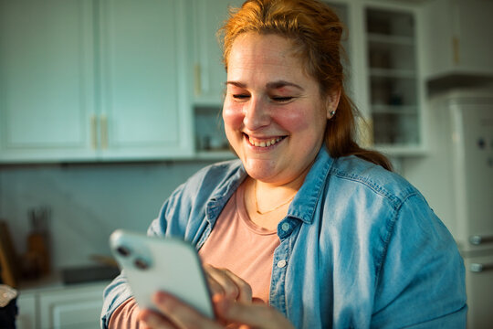 Smiling woman using smartphone in home kitchen