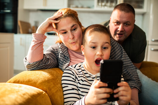 Surprised boy playing smartphone game with parents at home