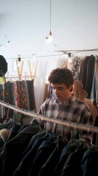 Young Man Examines Old Coats. Young Individual Browsing Retro Jackets Amid Bustling Store Shelves