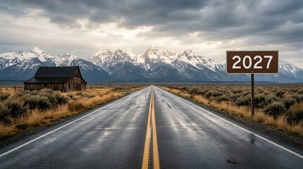 Obraz premium Scenic wet asphalt road leading toward snow covered mountain peaks under cloudy sky with roadside sign displaying year 2027 for conceptual transition.