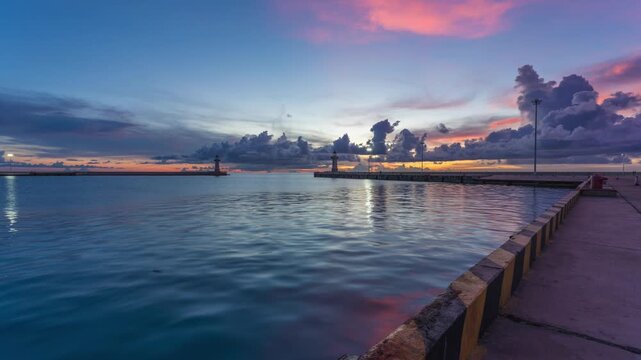 Calm Harbor at Sunset with Pier, Lighthouses, and Rippling Water