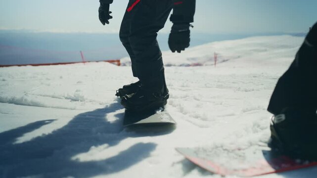 Two snowboarders are on a snow-covered mountain slope on a bright, sunny day. One snowboarder sits on the snow while the other stands nearby, ready for winter sports.