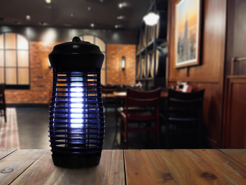 insects mosquito electric blue light killer lamp is put on nice wooden table in nice restaurant with background of wooden dinning table and chairs to protect repellent mosquito and other insects 