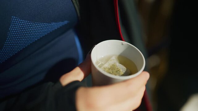 A person holds a warm mug with a steeping tea bag, enjoying a hot beverage. Hands are seen holding a comforting hot drink, ideal for winter or a relaxing break.