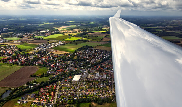 Glider wing soaring high above gifhorn, germany, with a patchwork of green fields and residential areas below