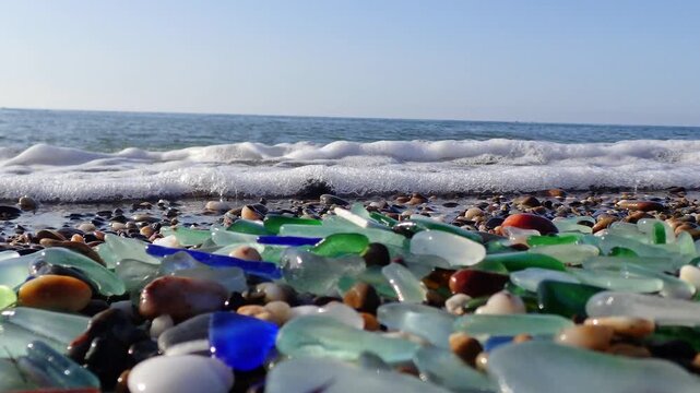 Colored sea glass with beach pebbles and shells in the mediterranean coast and in the background sea and waves with sunset and sky, sandy beach with coast glass, beach glass.