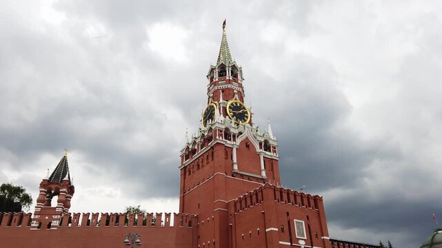 A static, low angle shot of Spasskaya Tower, part of Moscow Kremlin in Russia. The famous clock tower stands against a dramatic, heavy grey sky filled with clouds. A powerful architectural scene
